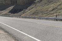 a biker riding down a street next to a canyon side highway with mountains and cliffs