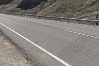 a biker riding down a street next to a canyon side highway with mountains and cliffs