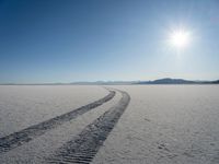 a truck tracks in a vast desert with mountains in the distance and a blue sky