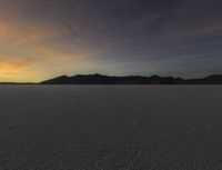 a sunset reflects in the horizon in a desert landscape, showing footprints from the ground