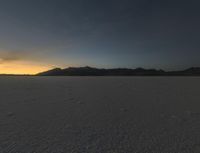 a sunset reflects in the horizon in a desert landscape, showing footprints from the ground