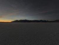 a sunset reflects in the horizon in a desert landscape, showing footprints from the ground