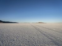 a lone desert scene, showing a vast plain, sky and distant mountains, some footprints of a person on the ground