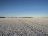 a lone desert scene, showing a vast plain, sky and distant mountains, some footprints of a person on the ground