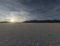 a sky is shown with tracks and a lone person on snow covered ground in front of mountain