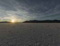 a sky is shown with tracks and a lone person on snow covered ground in front of mountain