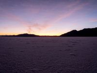 the sun is setting over a vast desert landscape with footprints left in it and mountains in the distance