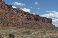 a horse stands on a dirt lot next to some rocky formations and a blue sky with clouds