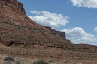 a horse stands on a dirt lot next to some rocky formations and a blue sky with clouds