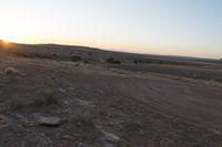 a motorcycle parked in the dirt near a hill and the sun sets on the horizon