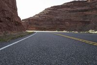 a person riding a motorcycle along a narrow road through rocks and sand cliffs a grassy area on both sides