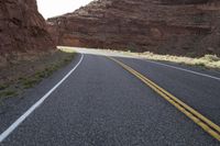 a person riding a motorcycle along a narrow road through rocks and sand cliffs a grassy area on both sides