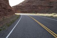 a person riding a motorcycle along a narrow road through rocks and sand cliffs a grassy area on both sides