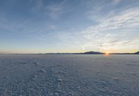 an ocean view of a large expanse of ice under a cloudy sky at sunset in the distance, mountains