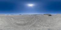 a desert landscape with sand, mountains and a sun in the middle of it from fisheye lens