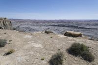 the arid landscape shows a very steep cliff with grass growing on it and shrubs in the foreground