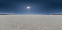 the sun over a wide, empty, plain desert in the distance is dark blue