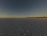 a plane flying through the sky on a plain with desert landscape in the background at sunset