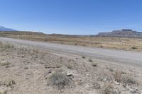 a road on a dirt field with rocks and grass next to a dirt road, two mountains in the distance