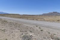 a road on a dirt field with rocks and grass next to a dirt road, two mountains in the distance