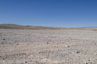 a lone car sits in a barren area next to a blue sky and dry terrain