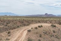 an image of a motorcycle driving on a dirt road in the desert under a cloudy sky