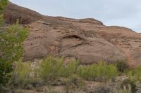 a motorcycle is traveling down a desert road near rocky hills, trees and bushes on the roadside