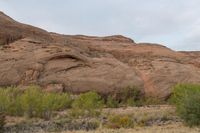 a motorcycle is traveling down a desert road near rocky hills, trees and bushes on the roadside