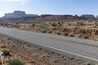 a man riding a motorcycle through desert next to mountains and a highway, with a single car driving alongside the road