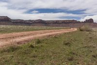 a dirt road in a barren area with a mountain backdrop in the distance and one large brown stone formation