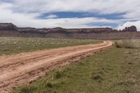 a dirt road in a barren area with a mountain backdrop in the distance and one large brown stone formation