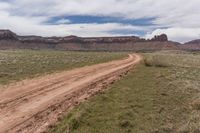 a dirt road in a barren area with a mountain backdrop in the distance and one large brown stone formation