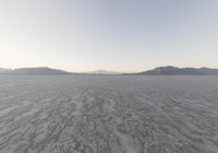 view of a barren plain with mountains in the distance while cloudy skies are above it