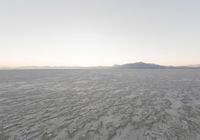 view of a barren plain with mountains in the distance while cloudy skies are above it