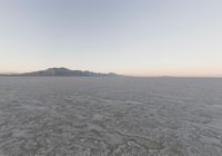 view of a barren plain with mountains in the distance while cloudy skies are above it