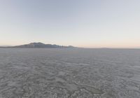 view of a barren plain with mountains in the distance while cloudy skies are above it