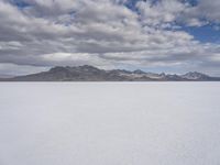 a snowy plain with mountains in the background and blue skies overhead with fluffy white clouds