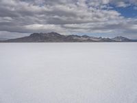 a snowy plain with mountains in the background and blue skies overhead with fluffy white clouds