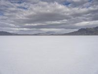 a snowy plain with mountains in the background and blue skies overhead with fluffy white clouds