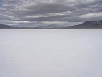 a snowy plain with mountains in the background and blue skies overhead with fluffy white clouds