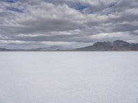 a snowy plain with mountains in the background and blue skies overhead with fluffy white clouds