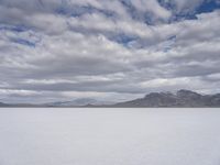 a snowy plain with mountains in the background and blue skies overhead with fluffy white clouds