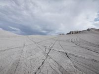 tracks and lines in the sand at a very large field with snow capped hills in the background