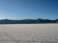 desert with mountains in background at the bottom of it and tire tracks on sand near the bottom of the ground