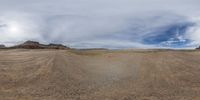 a 360 - camera image shows the desert with dirt roads and large mountains and clouds