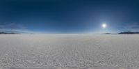 a panorama of snow and mountains in a desert field with clouds and sun shining through the sky