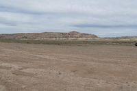 an empty field next to a big mountain with rocks in the background of the picture