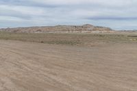 an empty field next to a big mountain with rocks in the background of the picture