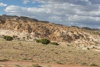 a truck driving in the desert under a partly cloudy sky, with mountains in the background