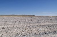 a lonely desert plain with small boulders and rocks in the foreground on a sunny day